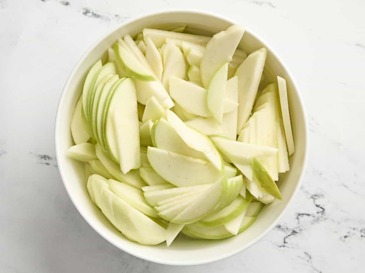 Sliced granny smith apples in a mixing bowl.