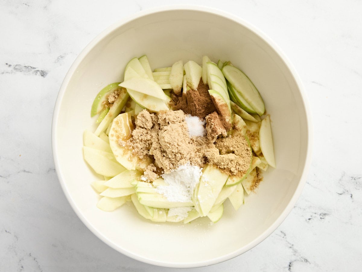 Sliced granny smith apples in a mixing bowl with sugar, cornstarch, and cinnamon.