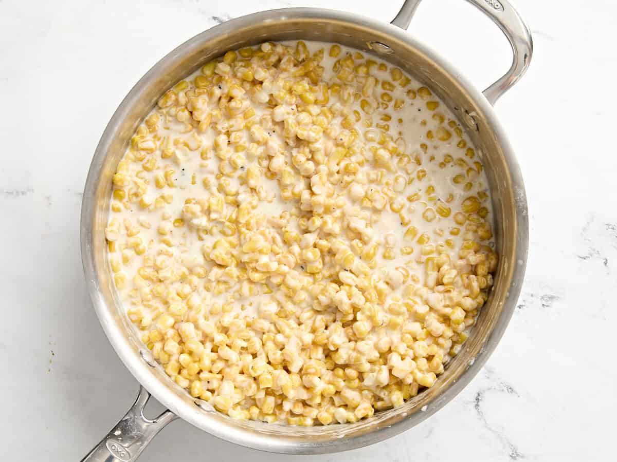 Corn kernels added to the cream sauce for creamed corn in a saucepan.