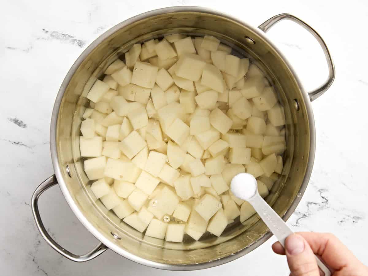 Diced potatoes in a pot of water with a spoon of salt being added.