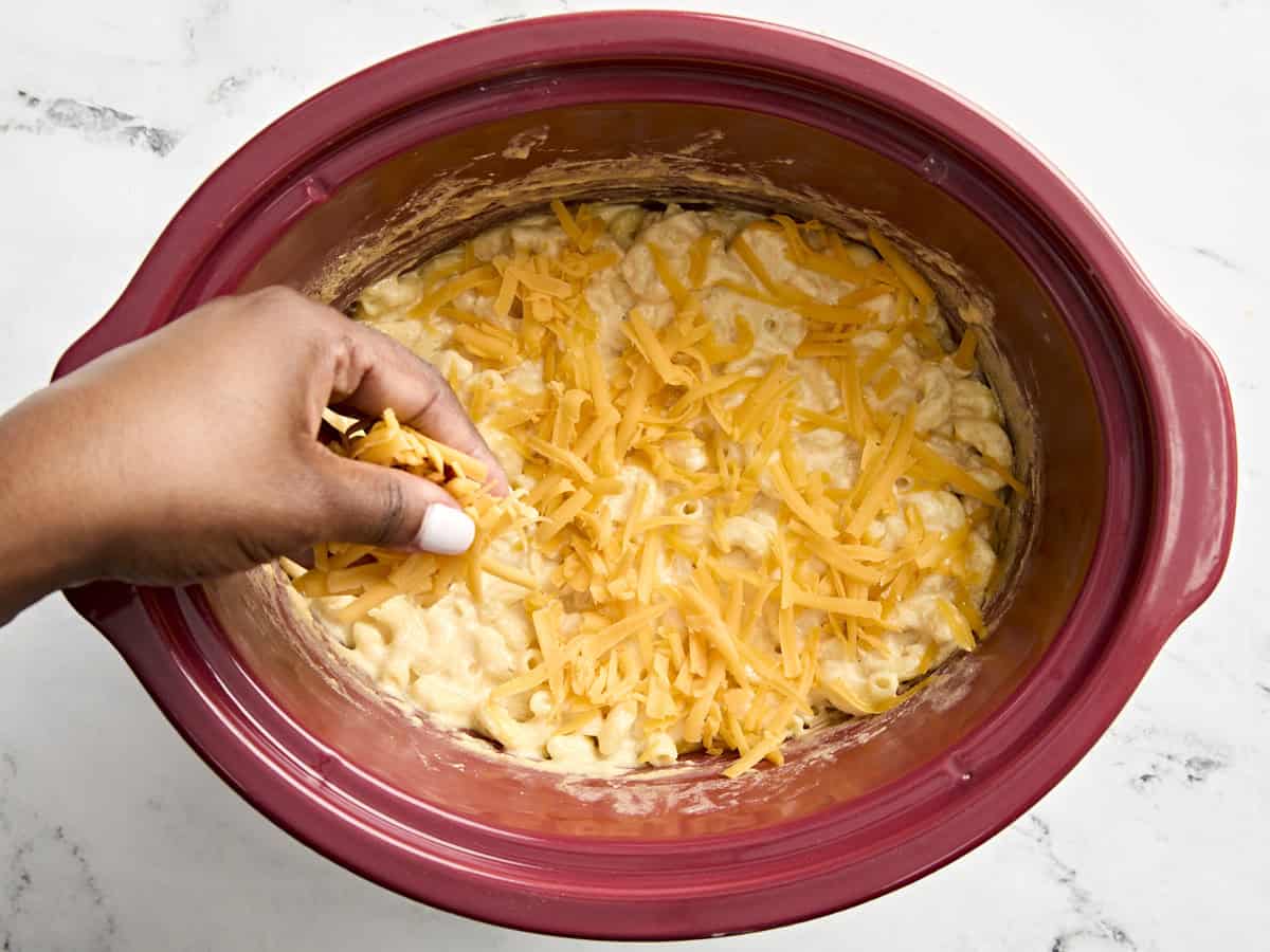 Adding shredded cheese on top of crockpot mac and cheese.