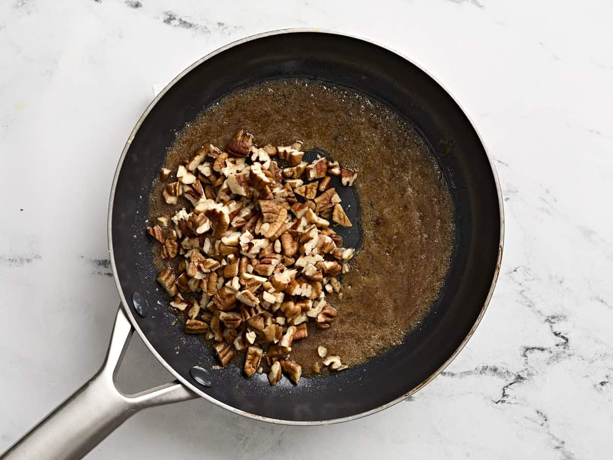 Sugar melted with chopped pecans in a skillet.