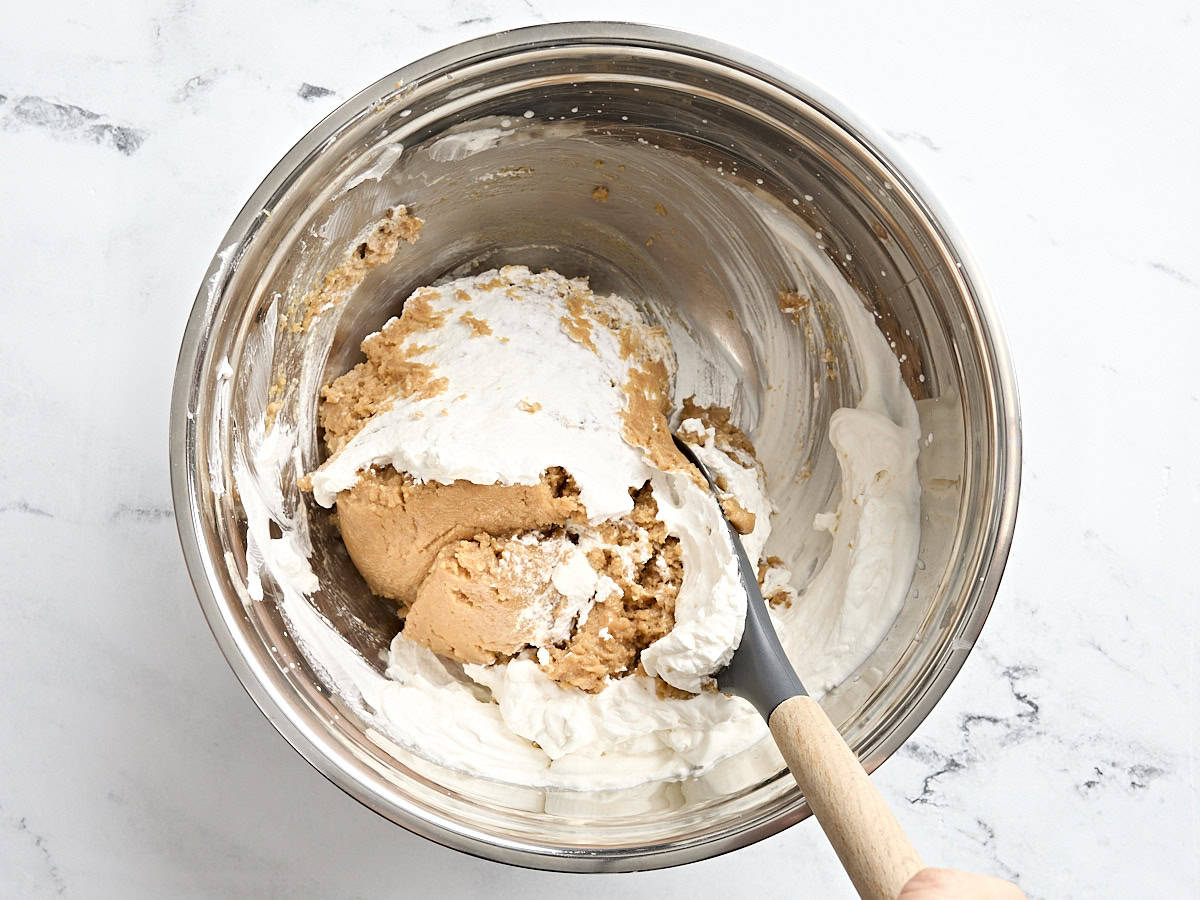 A spoon folding whipped cream and peanut butter pie filling together in a bowl.