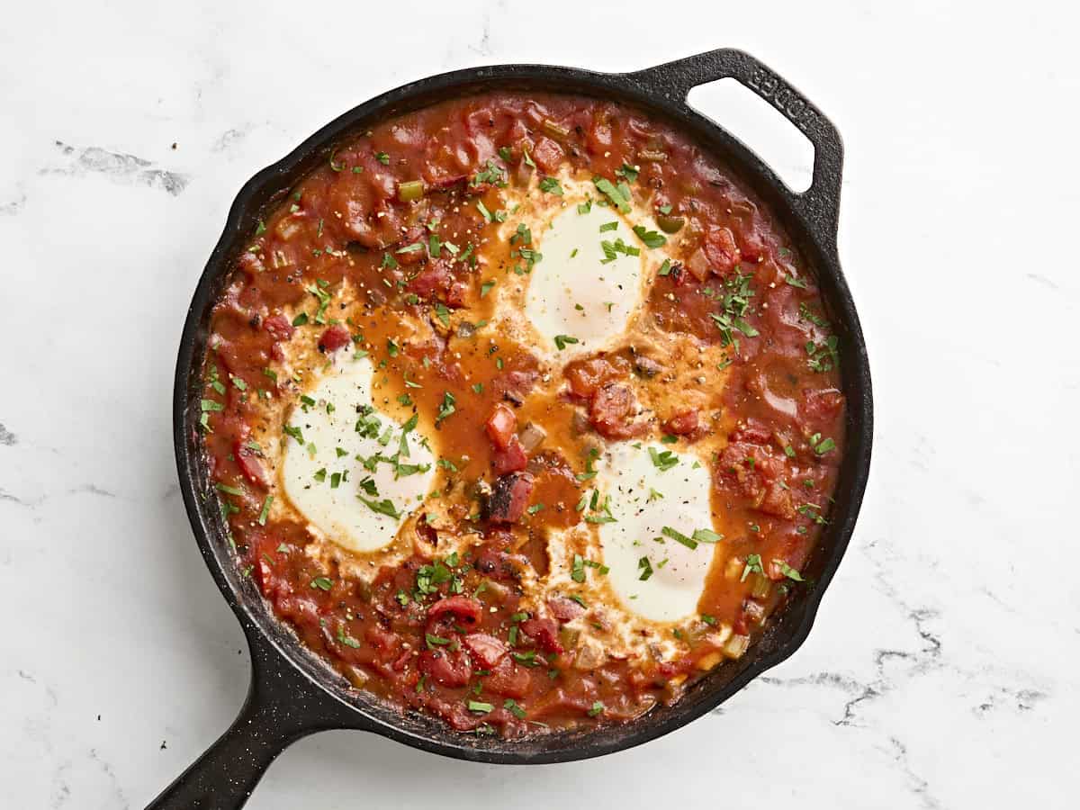 Finished shakshuka in a skillet, sprinkled with fresh parsley.