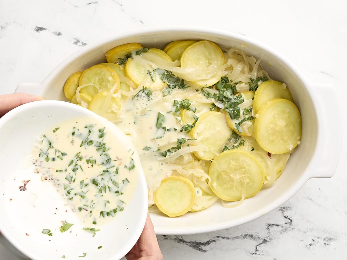 A bowl pouring cream sauce over squash casserole.