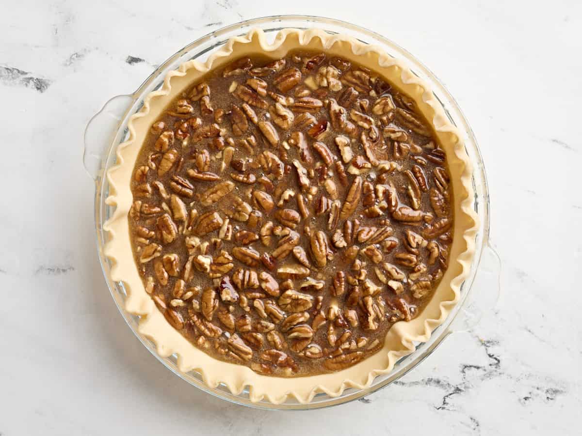 Pecan pie filling added to pie crust in a glass pie dish.