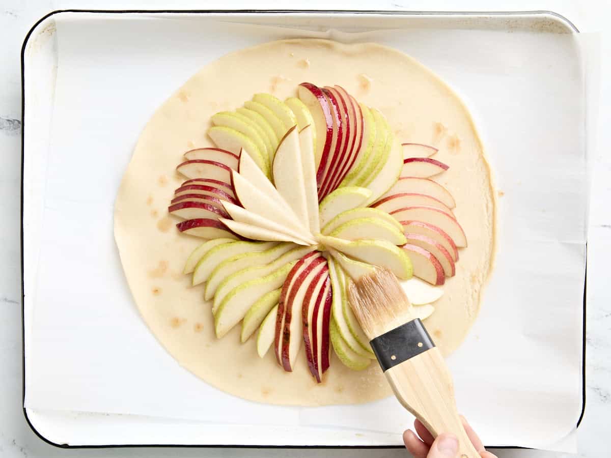 A brush glazing slices pears on a unbaked pre-made pie crust.