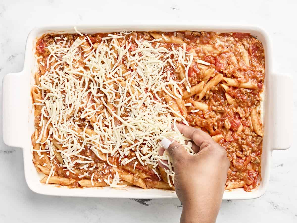 Mozzarella being added on top of mostaccioli pasta.