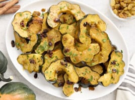 Roasted acorn squash with raisins and fresh parsley on a white serving platter.