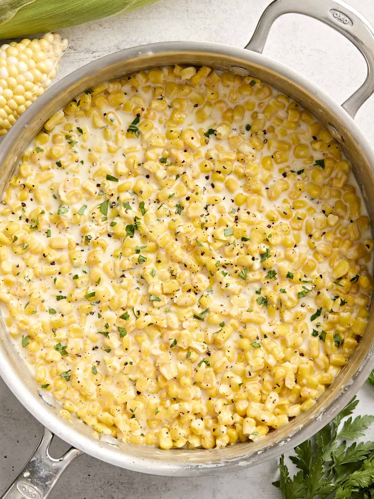 Overhead view of creamed corn in a sauce pan garnished with fresh parsley.