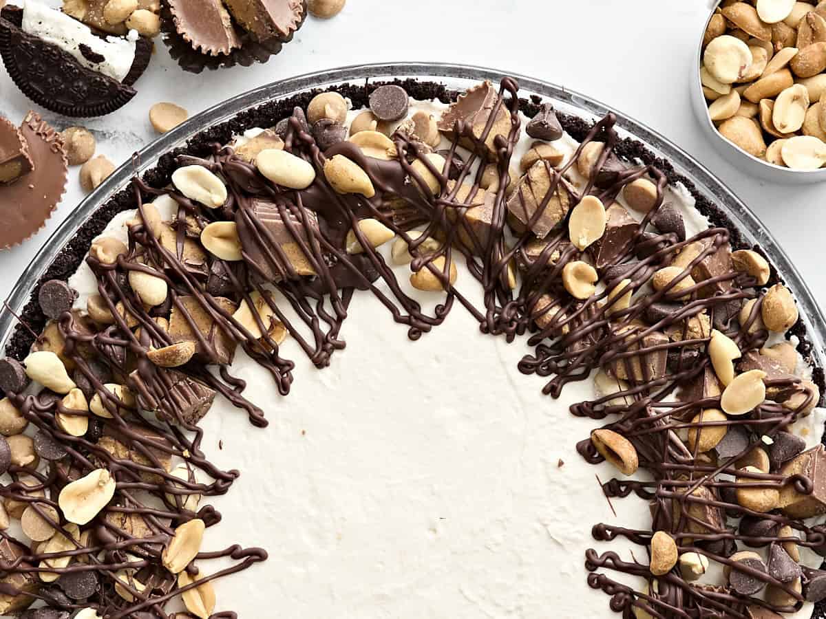 Overhead close up of a peanut butter pie decorated in melted chocolate, peanuts, and chopped peanut butter cups.