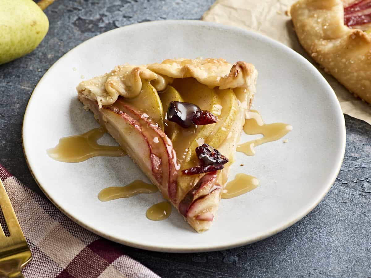 A slice of pear galette on a white plate, drizzled with caramel sauce.