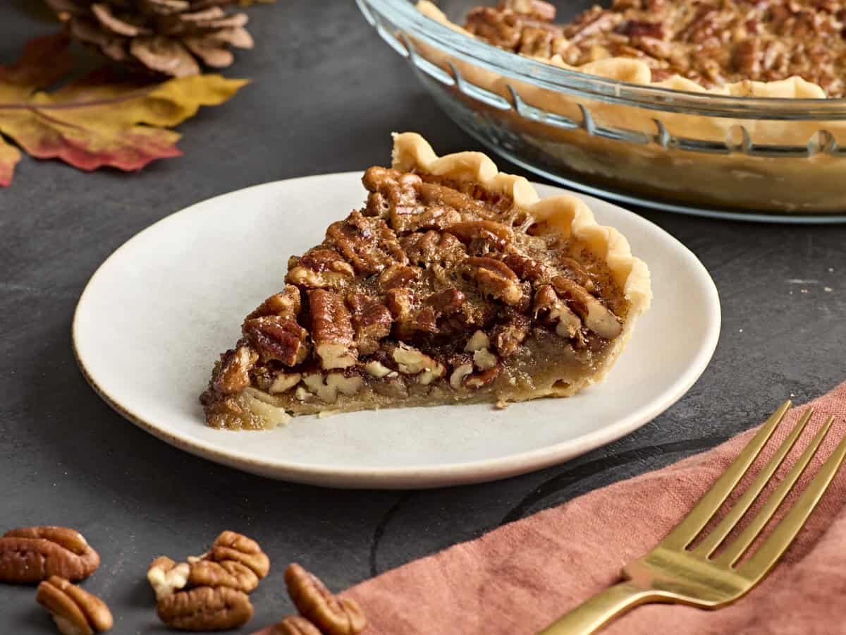 Side view of a slice of pecan pie on a white plate.