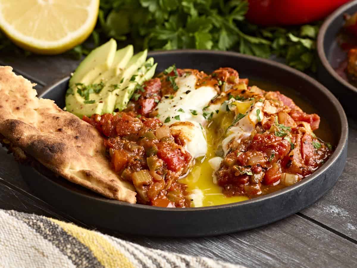 Side view of shakshuka on a plate with avocado and pita bread, with the yolk broken.