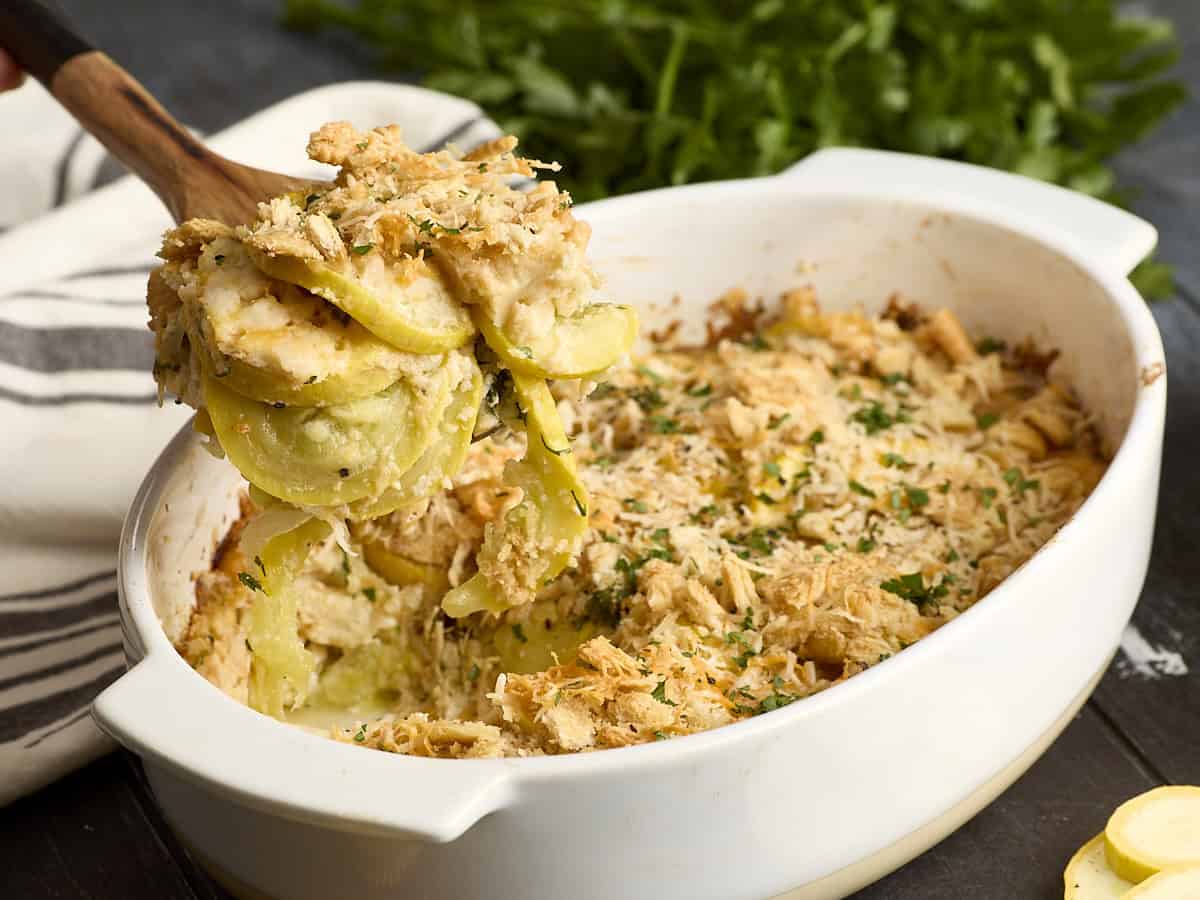 Side view of squash casserole being scooped out of a casserole dish with a wooden spoon.