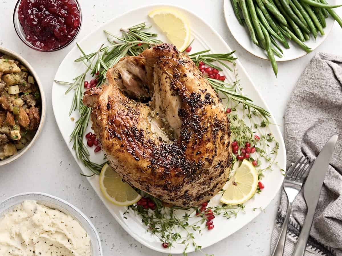 overhead view of a roasted turkey breast on a white platter with thanksgiving sides around the platter.