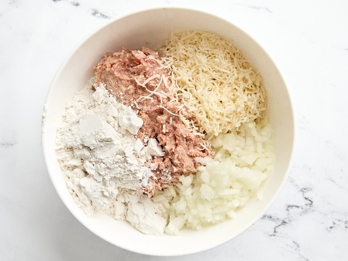 Diced onions, pancake mix, ground sausage, and shredded cheese for sausage balls in a mixing bowl.