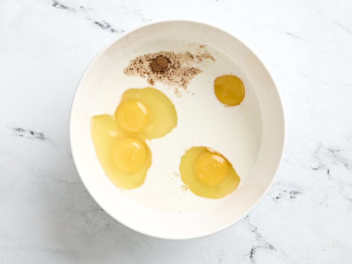 Cinnamon, eggs, milk,  and condensed milk in a mixing bowl.