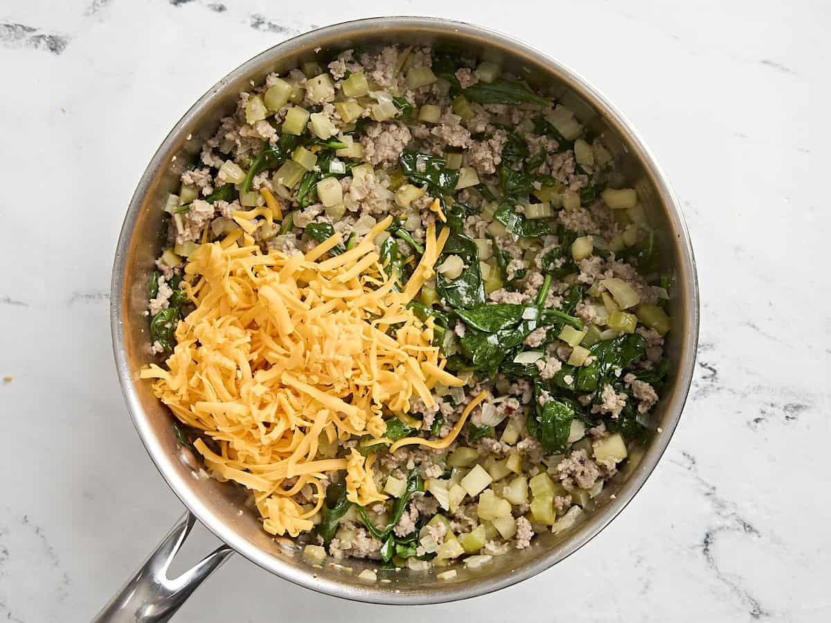 Shredded cheddar added to stuffing mixture for stuffed butternut squash in a pan.