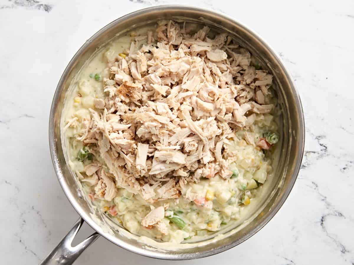 Shredded turkey added to the ingredients for turkey pot pie in a sauce pan.