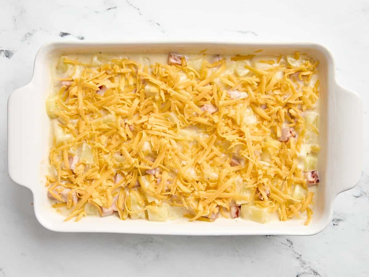 Ham and potato casserole topped with shredded cheese in a casserole dish.