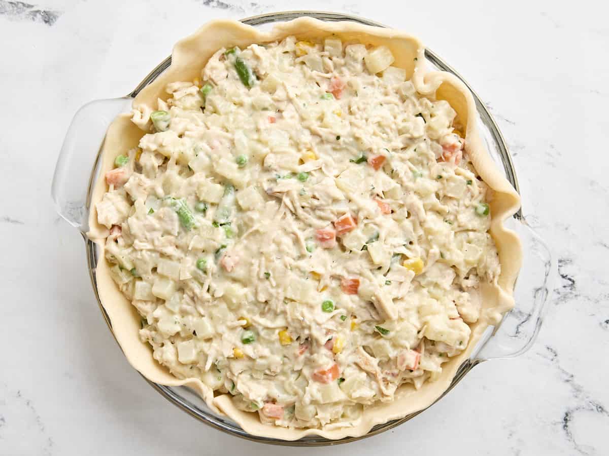 Turkey pot pie filling added to the rolled out crust in a pie pan.