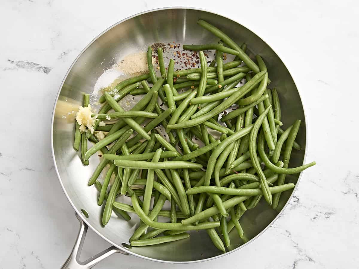 Green beans in a skillet with minced garlic and seasonings.