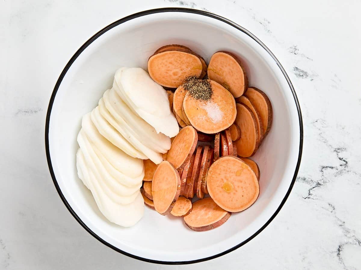 Sliced turnip and sweet potato in a bowl with salt and pepper.