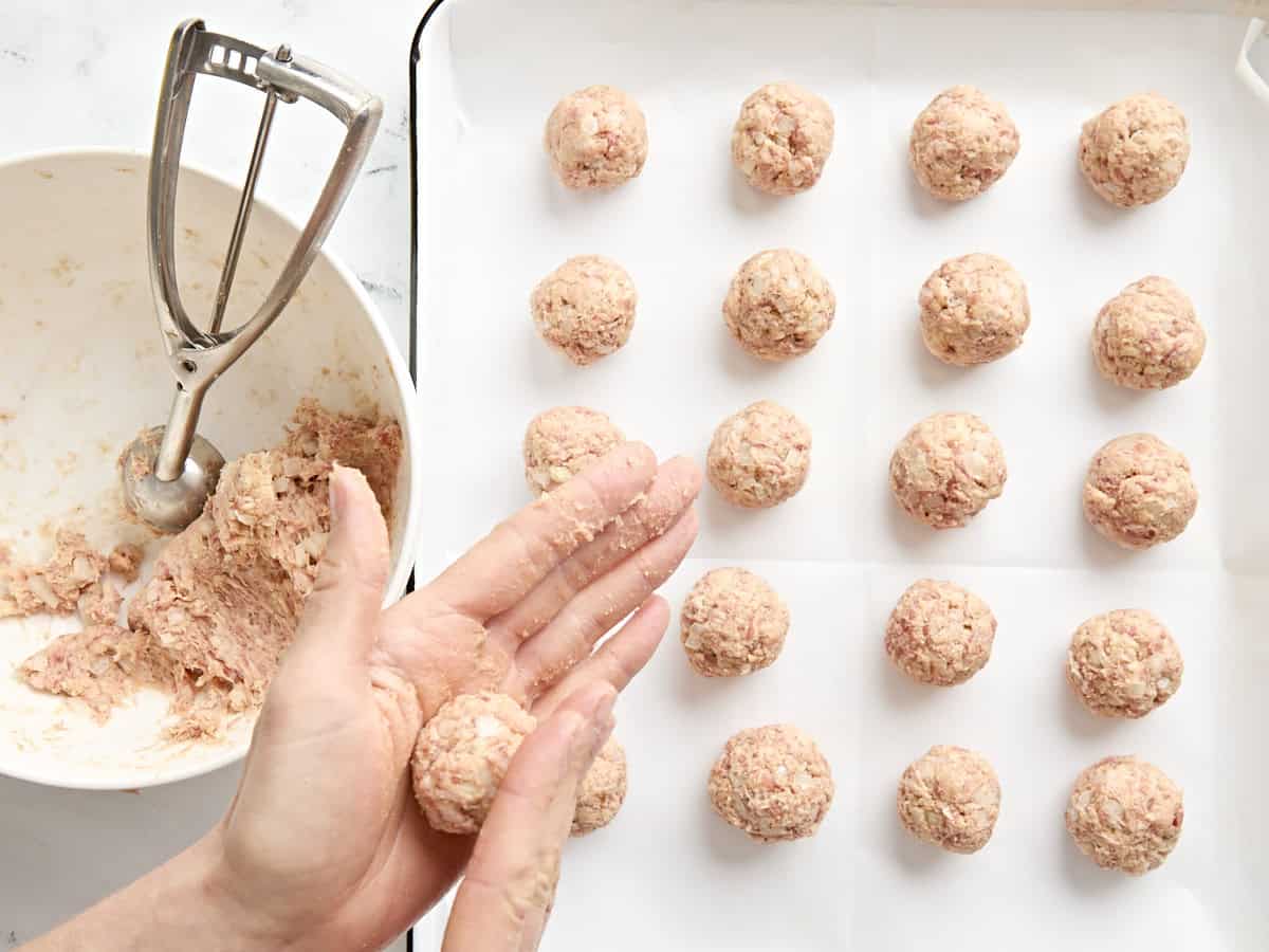 A hand rolling sausage ball meat over a tray of uncooked sausage balls.