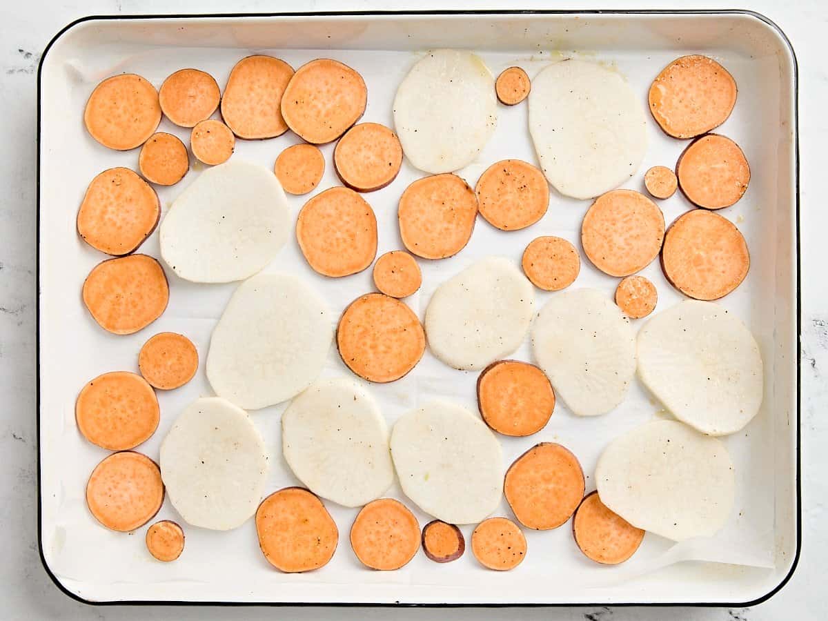 Sliced potatoes and turnips on a baking sheet.