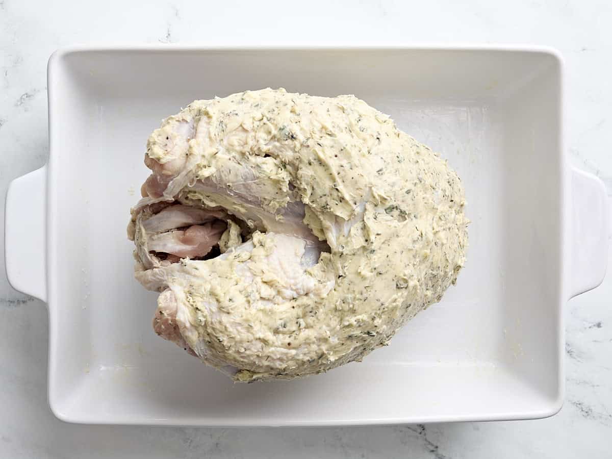 Turkey breast fully covered with herb butter placed inside a large baking dish.