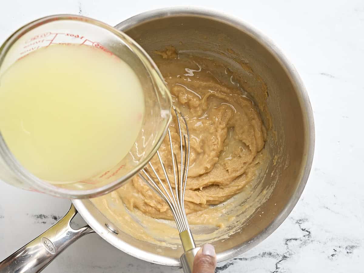 A hand whisking turkey broth into a golden roux in a saucepan to make turkey gravy.