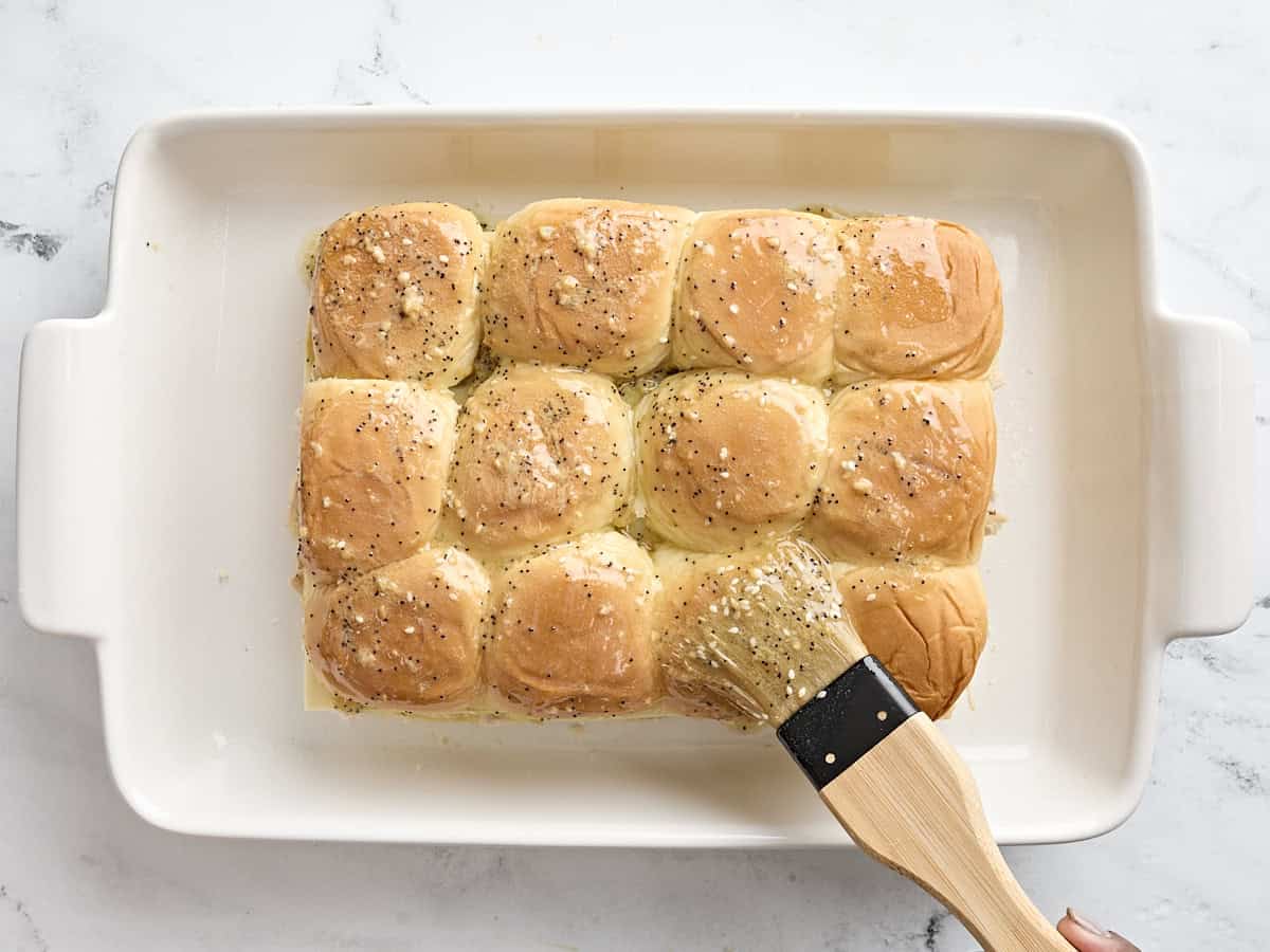 A brushed coating the top of turkey slider rolls with melted butter and seasonings.