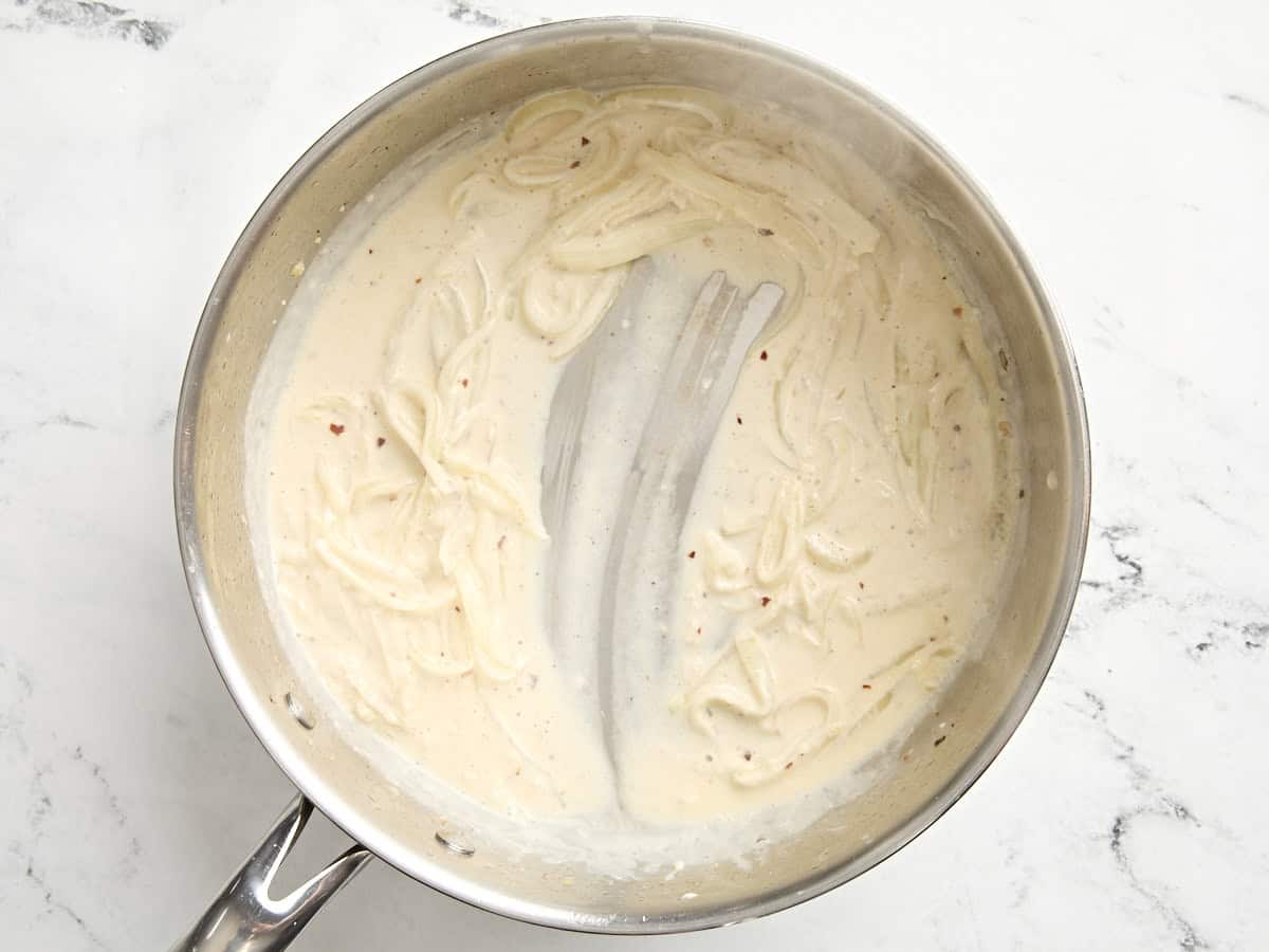 Creamy onion sauce for creamed kale in a skillet.