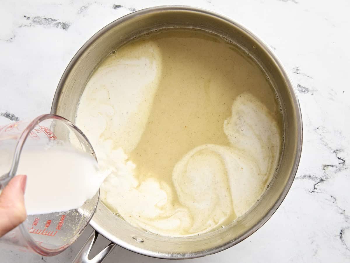 Half and half added to the creamy sauce for turkey pot pie in a saucepan.