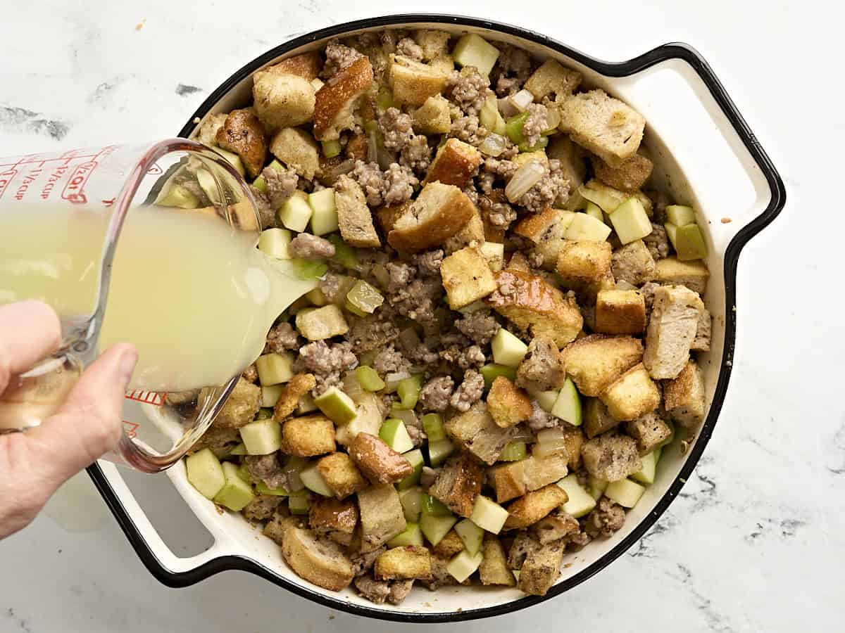 Chicken bouillon being poured into sausage stuffing in a casserole dish.