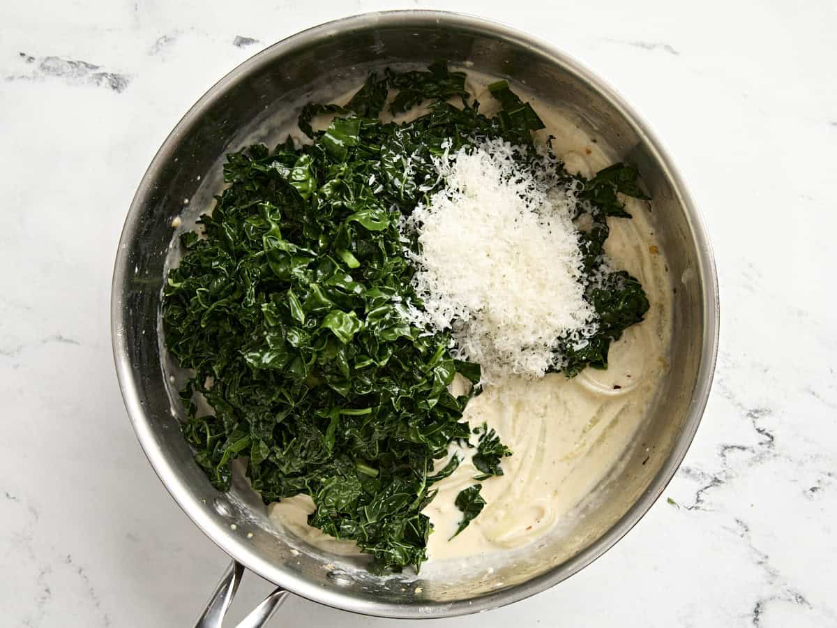 Blanched kale with parmesan cheese added to a creamy sauce in a skillet.