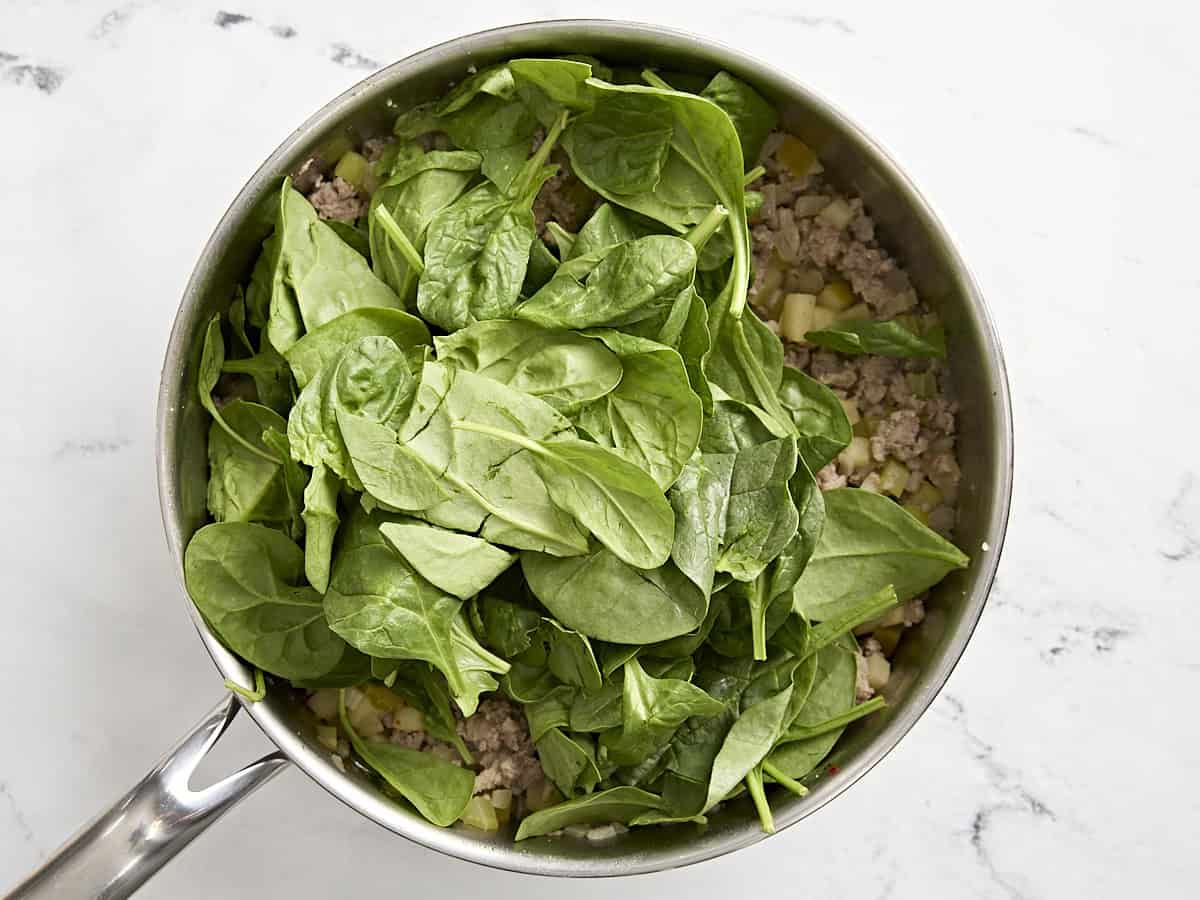 Spinach added to ground sausage mixture in a pan.