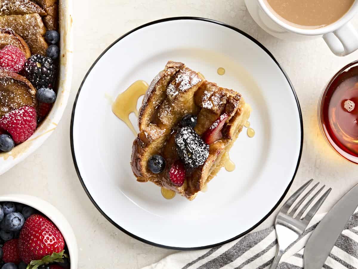 Overhead view of a slice of baked french toast on a white plate, drizzled with maple syrup.