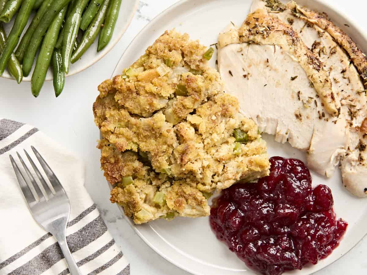 Overhead view of a serving plate with roasted turkey, corbread dressing, and cranberry sauce.