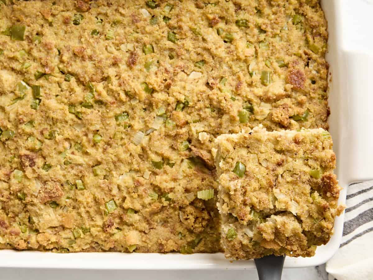 overhead view of a serving of cornbread dressing being lifted out of a white baking dish.