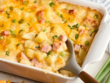 A serving spoon scooping ham and potato casserole from a baking dish.