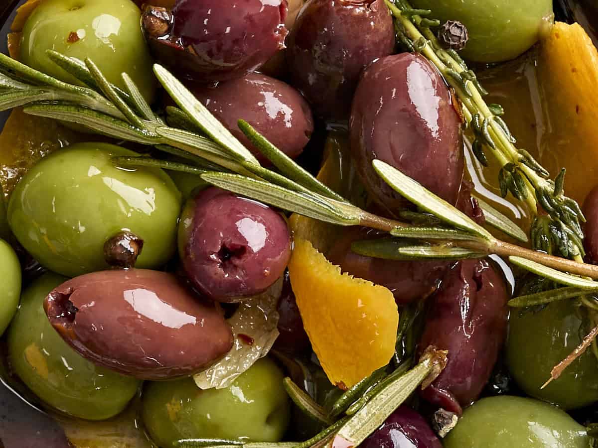 Close up of marinated olives and fresh herbs.