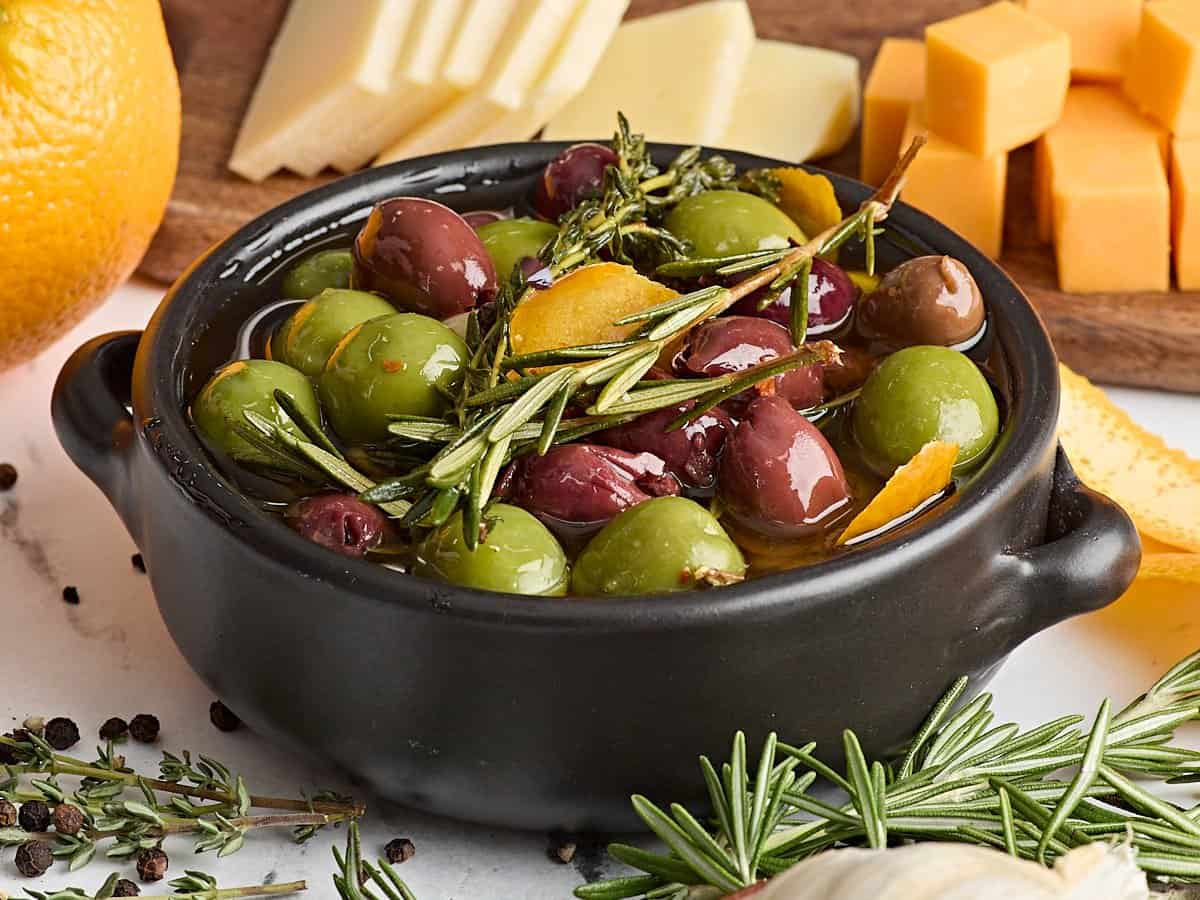 Side view of marinated olives with fresh herbs.