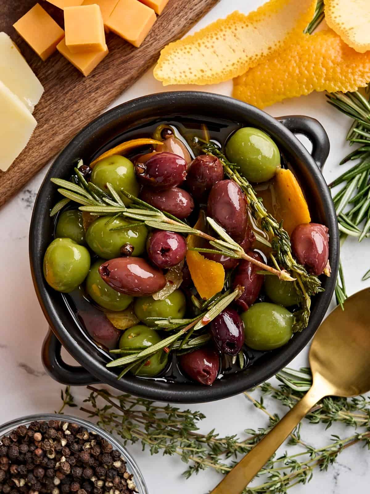 Overhead view of a bowl of marinated olives with fresh herbs.