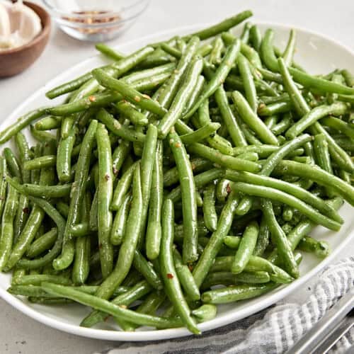 Side view of sauteed green beans on a white serving platter.