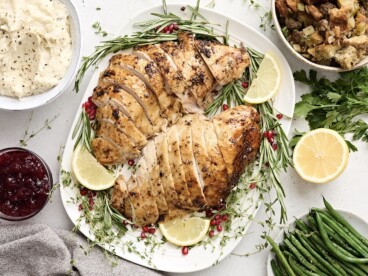 Overhead view of sliced turkey breast on a platter with fresh herbs and lemon slices as a garnish.