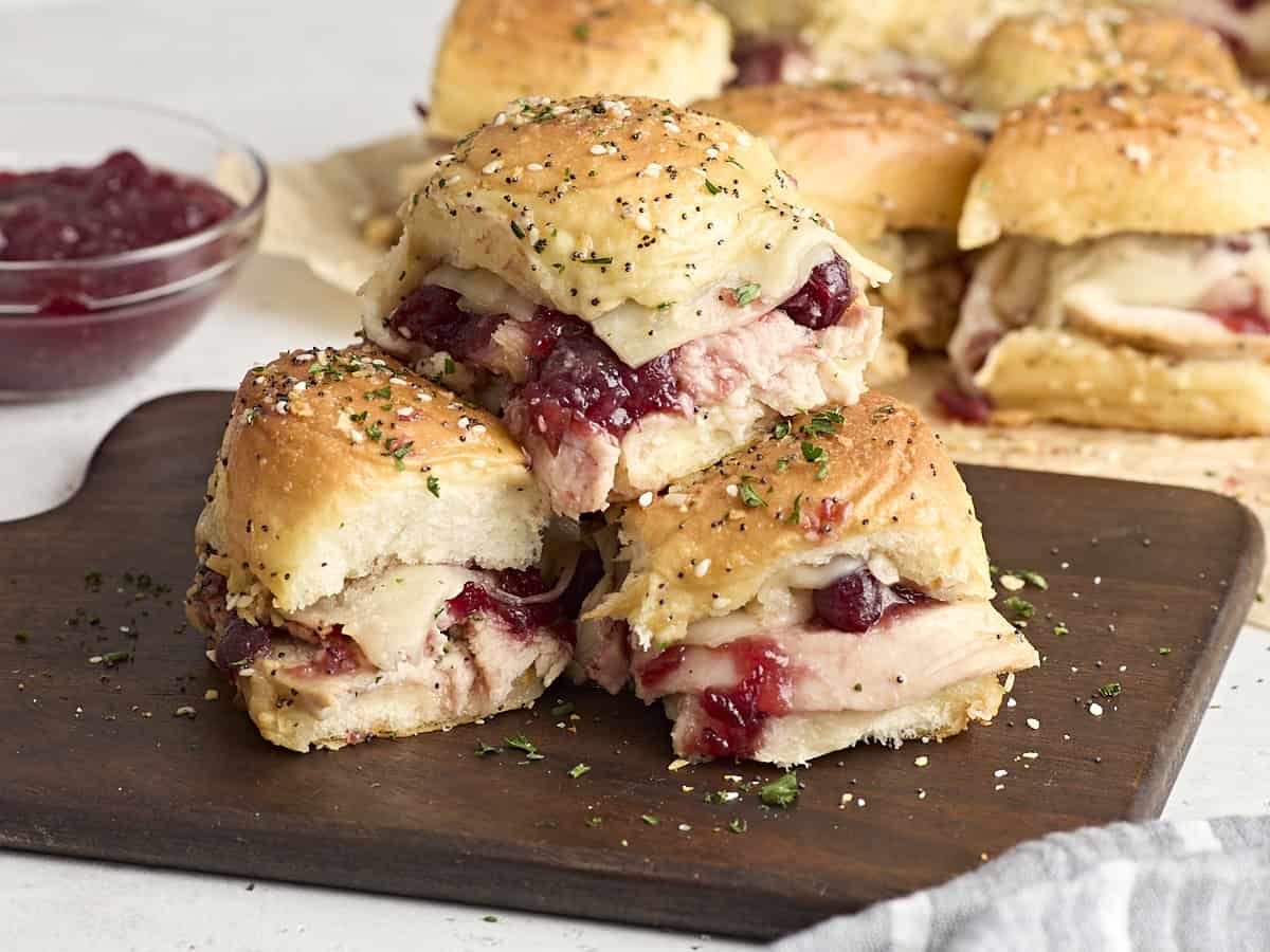 A stack of turkey sliders with cranberry sauce on a wooden chopping board.