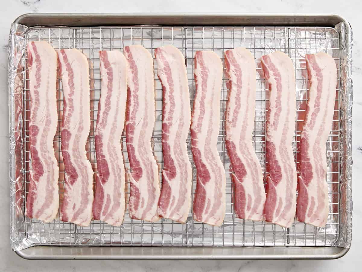 Slices of bacon on a wire rack over a baking sheet.