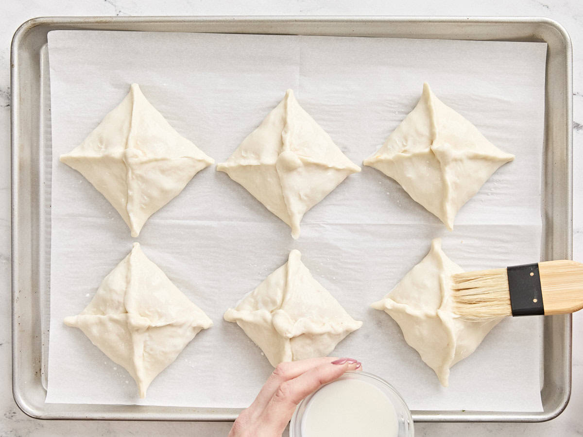 A brush adding a milk wash to the tops of unbaked sausage and cheese hand pies.